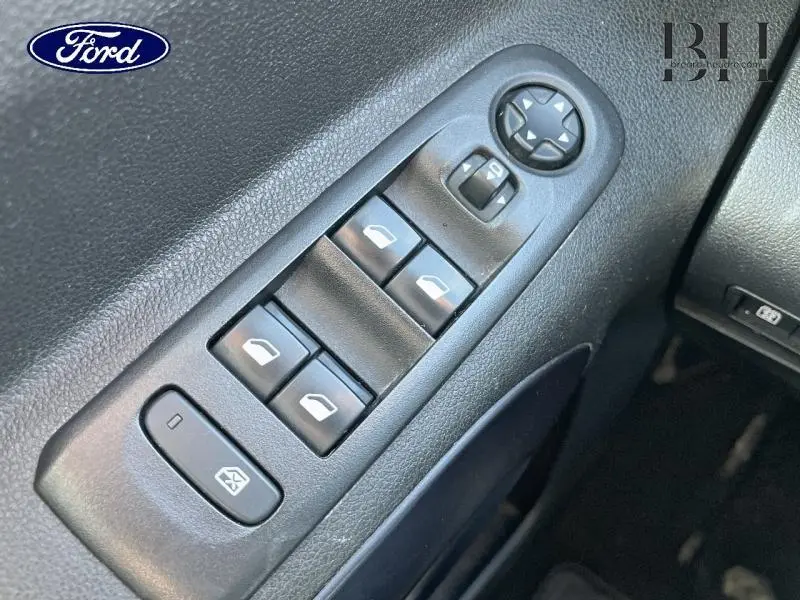 Gros plan sur les commandes des vitres électriques et rétroviseurs sur la porte intérieure noire d’un véhicule.