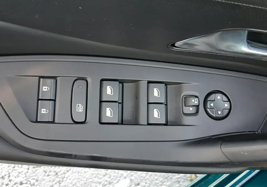 Vue rapprochée des commandes de lève-vitres et rétroviseurs sur la porte côté conducteur d'une Peugeot 308 Bleu Obsession.
