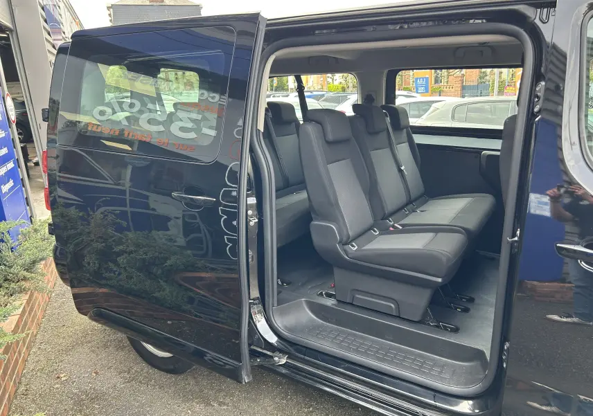 Vue latérale droite d’un Opel Vivaro Combi noir avec porte coulissante ouverte montrant les sièges passagers en tissu.