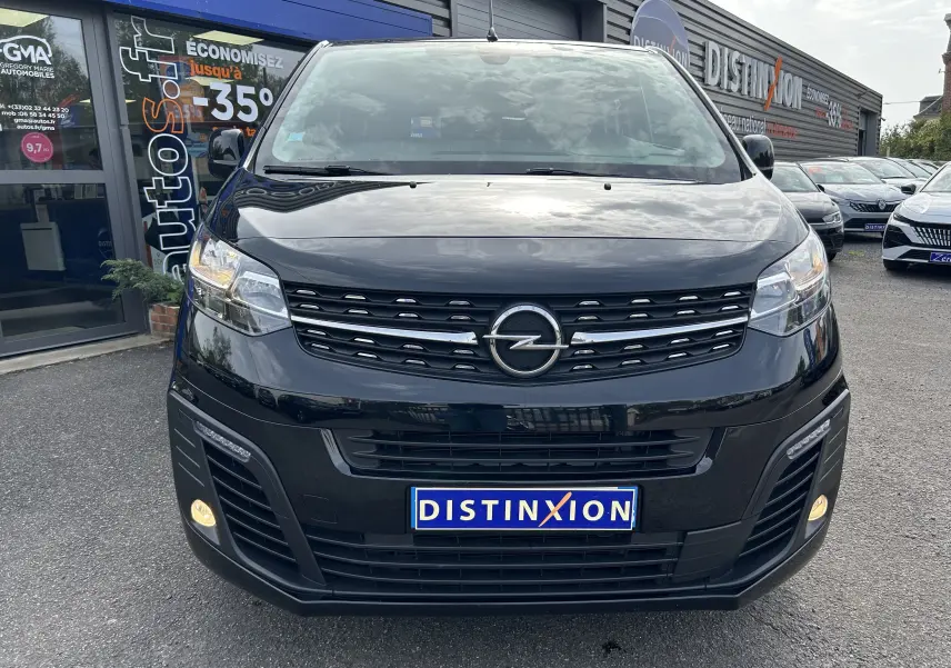 Vue avant d'un Opel Vivaro Combi noir 2022 avec calandre distinctive et phares allumés, stationné devant un concessionnaire.