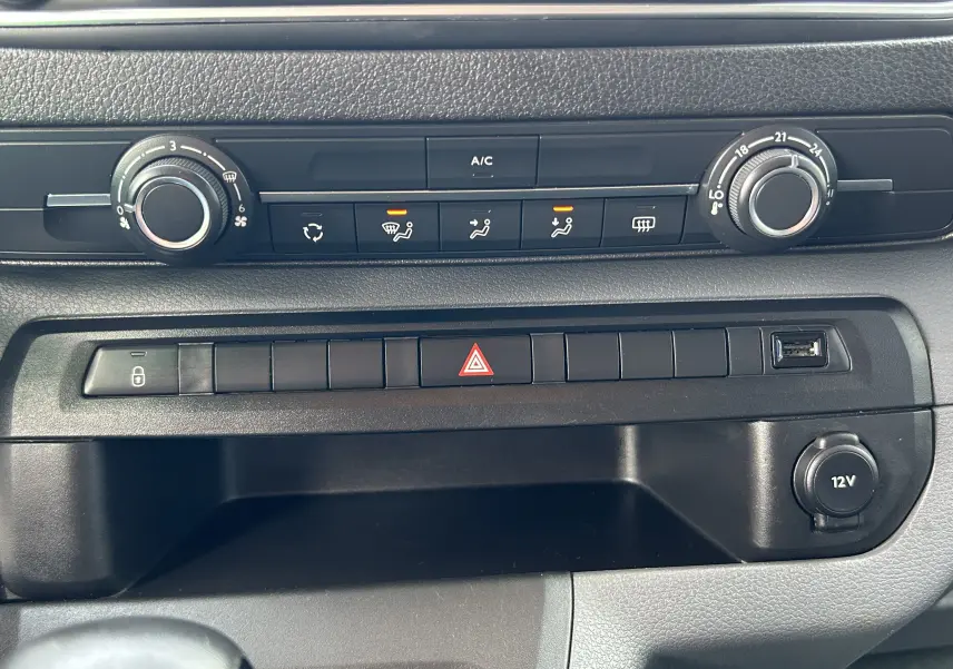 Vue rapprochée de la console centrale noire de l'Opel Vivaro Combi 2022 avec commandes de climatisation et prise 12V.