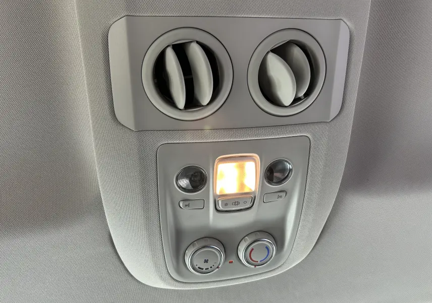 Vue intérieure en gros plan du plafonnier gris avec commandes de climatisation et éclairage allumé dans un Opel Vivaro Combi noir.