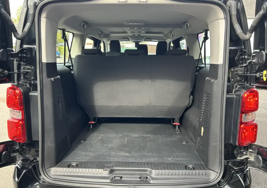 Vue arrière du coffre ouvert d’un Opel Vivaro Combi noir, montrant l’espace de chargement et la banquette arrière.