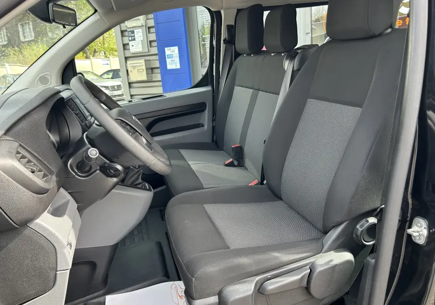 Vue intérieure côté conducteur de l’Opel Vivaro Combi noir 2022, montrant les sièges tissu bicolore et le volant.
