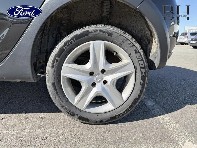 Gros plan sur la roue avant droite d'une Dacia Sandero noir nacré avec jante étoile cinq branches.