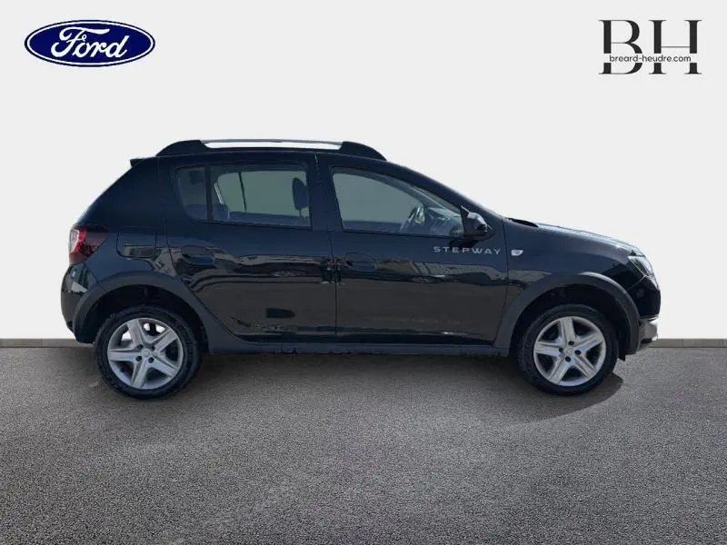 Profil droit d'une Dacia Sandero Stepway noire nacrée de 2016 avec barres de toit et jantes alliage visibles.