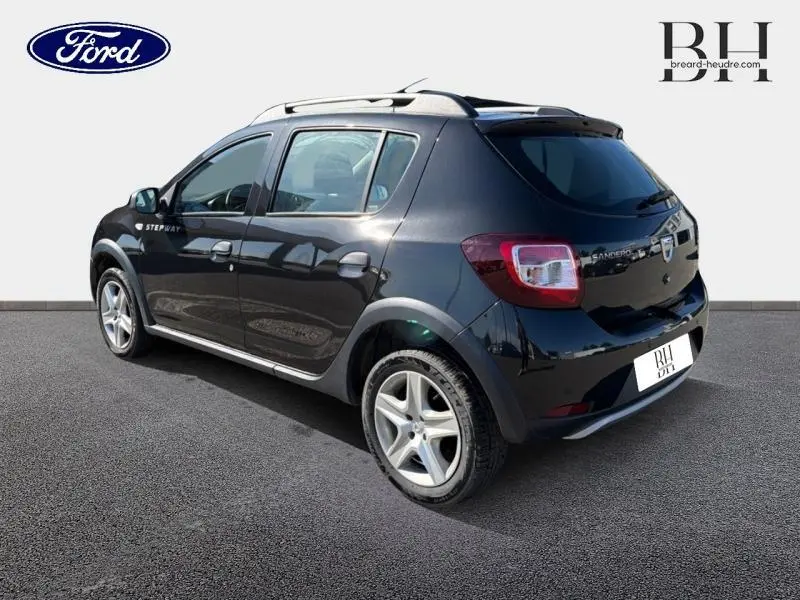 Vue 3/4 arrière droite d'une Dacia Sandero Stepway 2016 noir nacré avec barres de toit et jantes alliage.