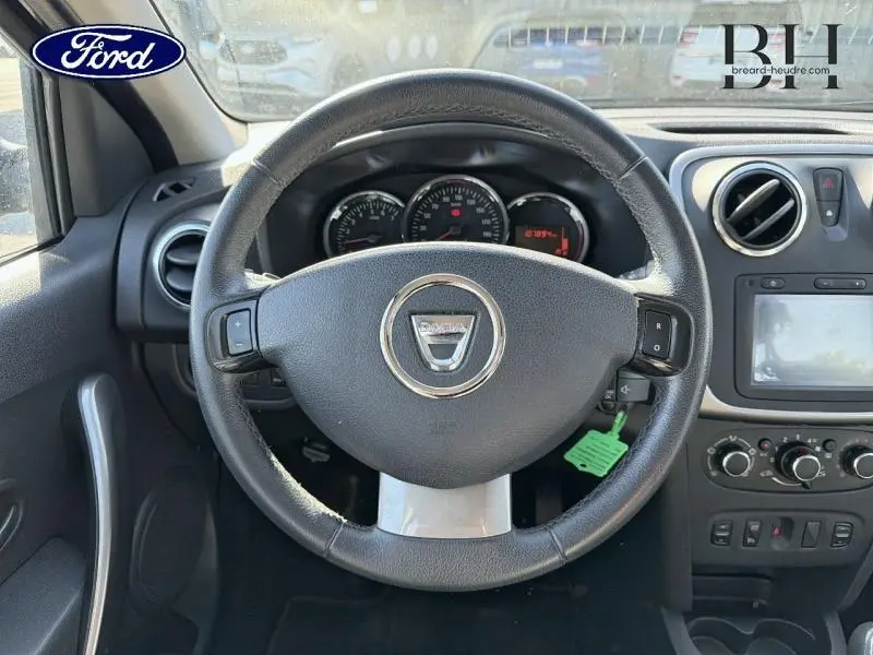 Vue intérieure centrée sur le volant cuir de la Dacia Sandero noir nacré avec tableau de bord et écran tactile visibles.