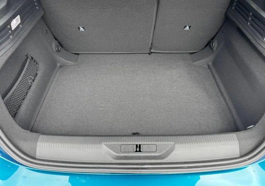 Coffre vide vu de dessus d'une Peugeot 308 1.2 Hybrid bleu, montrant la moquette et les rangements latéraux.