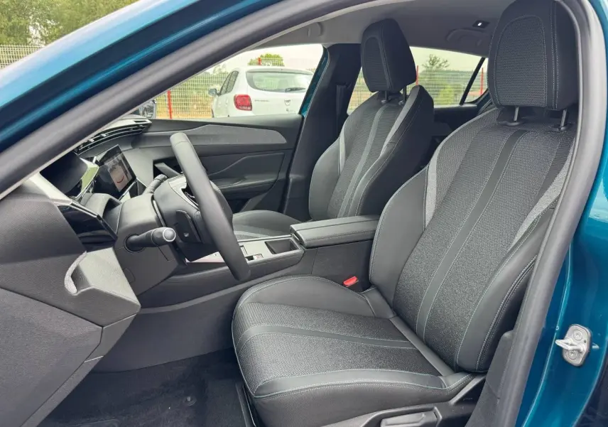 Vue intérieure côté conducteur de la Peugeot 308 bleu, sièges en tissu et cuir avec console centrale et volant multifonction.