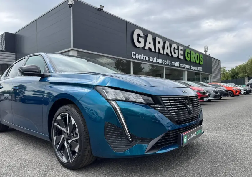 PEUGEOT 308 bleu 3/4 avant droit avec calandre noire et feux LED, devant un garage automobile.