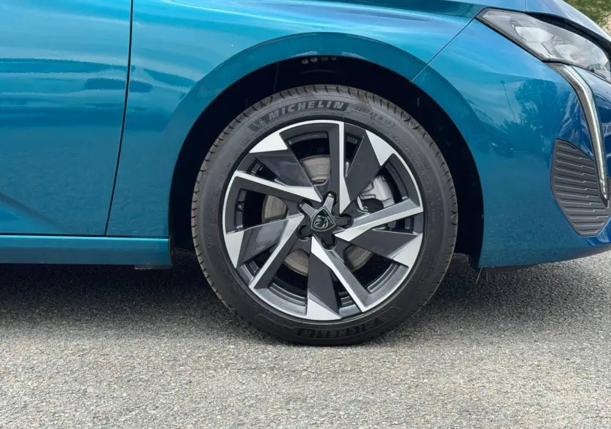 Gros plan sur la roue avant gauche et partie latérale d’une Peugeot 308 bleu Obsession avec jante alu stylisée.