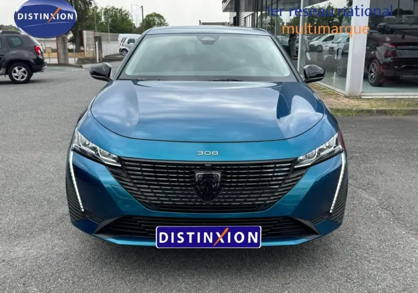 Vue avant d'une Peugeot 308 bleu Obsession 2025 avec calandre noire et feux LED verticaux allumés.