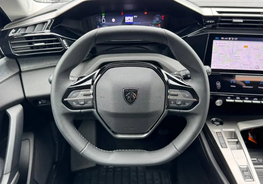 Vue frontale du volant cuir noir de la Peugeot 308 1.2 Hybrid 145ch avec tableau de bord numérique et écran tactile.