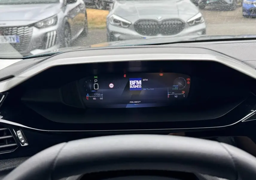 Vue intérieure du tableau de bord numérique de la Peugeot 308 bleu, affichant la radio BFM Business et les indicateurs de conduite.
