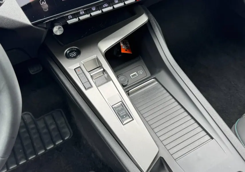 Vue rapprochée de la console centrale grise avec levier de vitesses et bouton start/stop du Peugeot 308 hybride 2025.