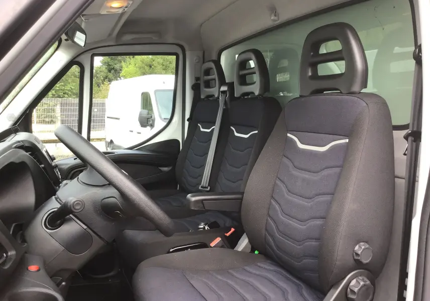 Vue intérieure côté conducteur de l'Iveco Daily Chassis Cabine 2022, sièges noirs avec appuie-têtes et volant visible.