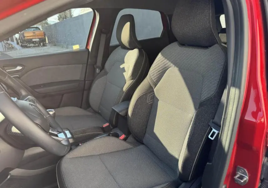 Vue intérieure côté conducteur du Renault Captur rouge flamme, sièges tissu gris avec accoudoir central.