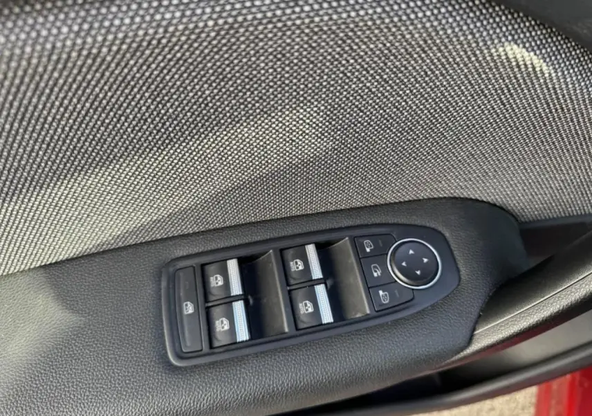 Gros plan sur les commandes des vitres électriques et rétroviseurs sur la porte côté conducteur du Renault Captur rouge flamme.