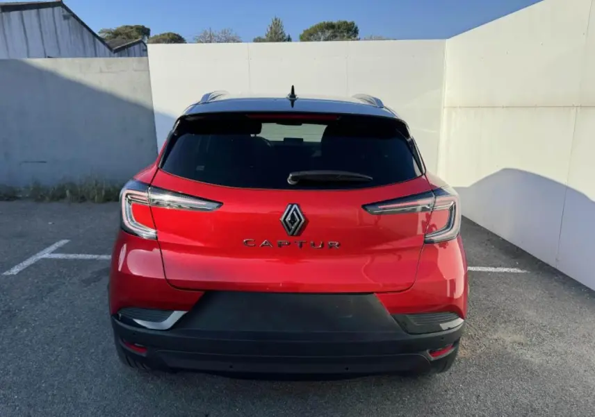Vue arrière d'un Renault Captur rouge flamme avec toit noir, feux LED et logo central bien visible.