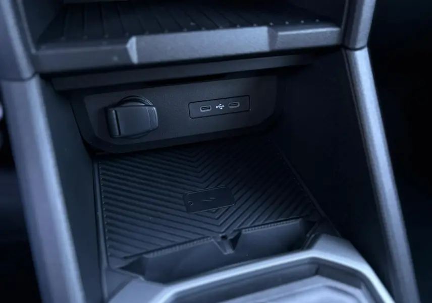Gros plan sur la console centrale du Dacia Duster gris, montrant le chargeur à induction et ports USB-C.