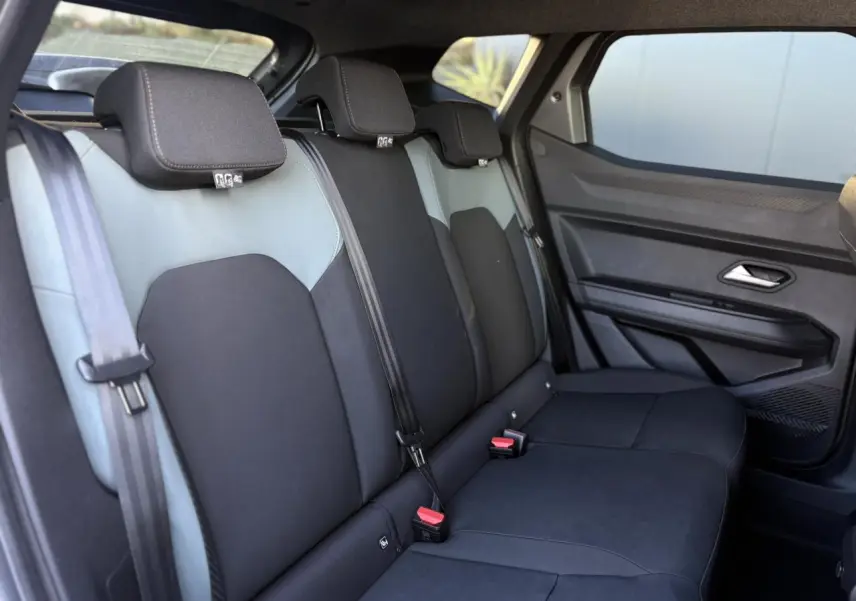 Vue latérale droite sur la banquette arrière bicolore gris et noir du Dacia Duster 2025, avec appuie-têtes et ceintures visibles.