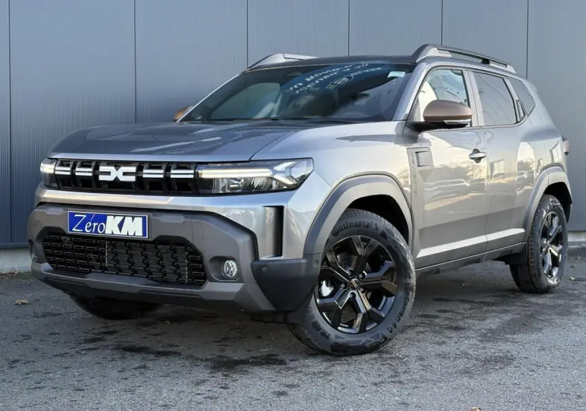 Dacia Duster 2025 gris schiste en 3/4 avant droit, jantes noires et coques de rétroviseur brun cuivré visibles.