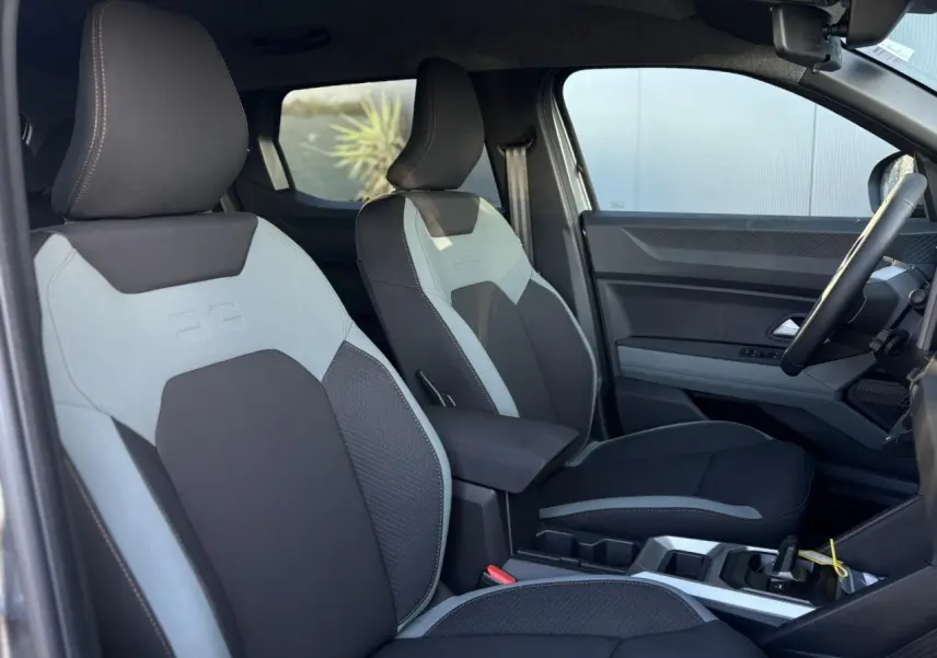 Vue intérieure côté droit du Dacia Duster 2025, sièges bicolores gris clair et noir avec accoudoir central.