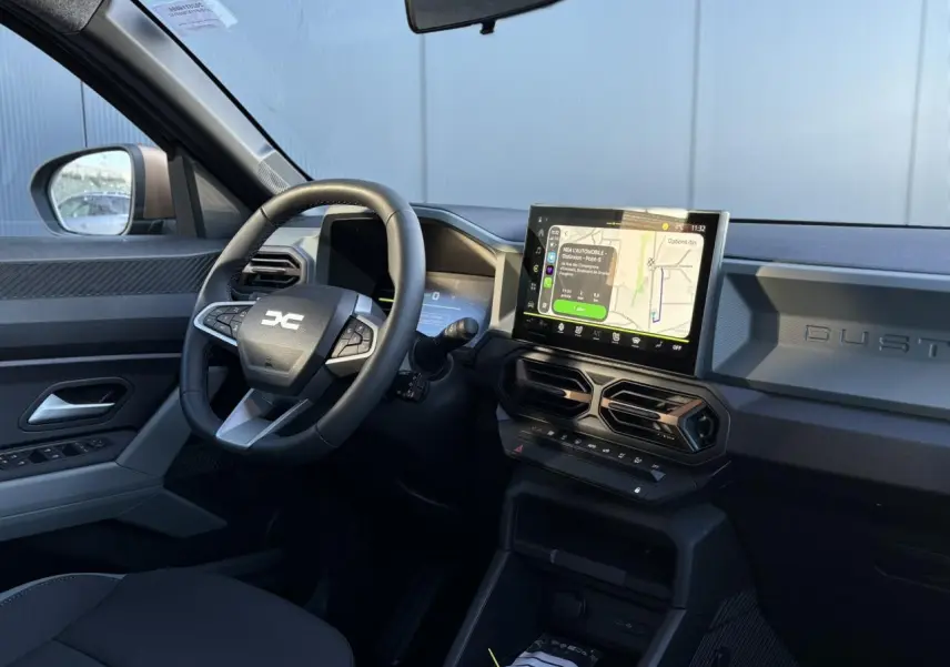 Intérieur du Dacia Duster 2025 gris, vue côté conducteur, tableau de bord avec écran tactile GPS et volant multifonction.