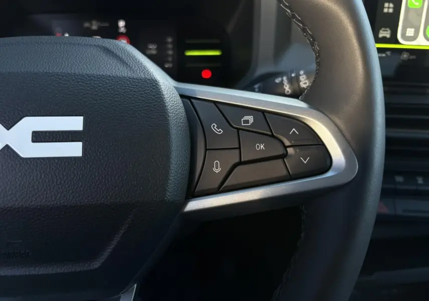Gros plan sur le côté droit du volant noir du Dacia Duster 2025 avec commandes multifonctions et détails argentés.