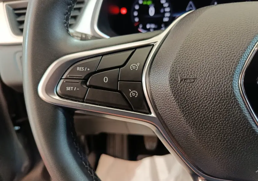 Gros plan sur les commandes du volant noir du Renault Captur Techno TCe 90 2024, avec affichage numérique flou en arrière-plan.