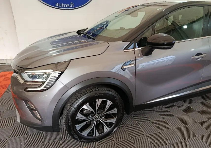 Vue de profil avant droit d'un Renault Captur techno TCe 90 gris foncé avec jante alliage et rétroviseur noir brillant.