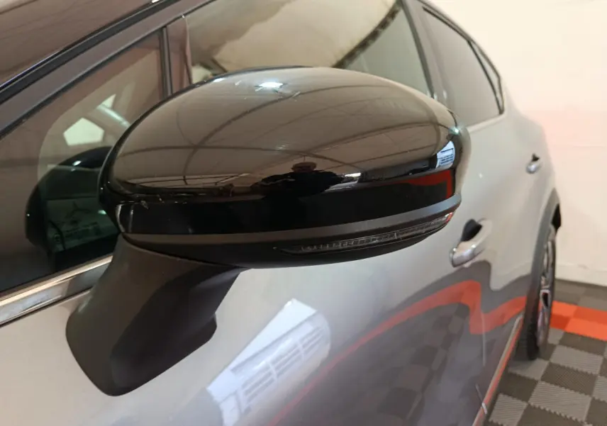 Gros plan sur le rétroviseur noir côté gauche du Renault Captur gris foncé 2024, avec reflet de l'environnement intérieur.