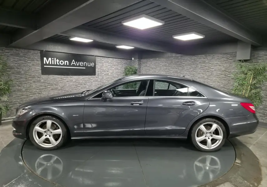 Profil côté gauche d'une Mercedes CLS 250 CDI gris métallisé avec jantes alliage 5 branches en intérieur showroom.
