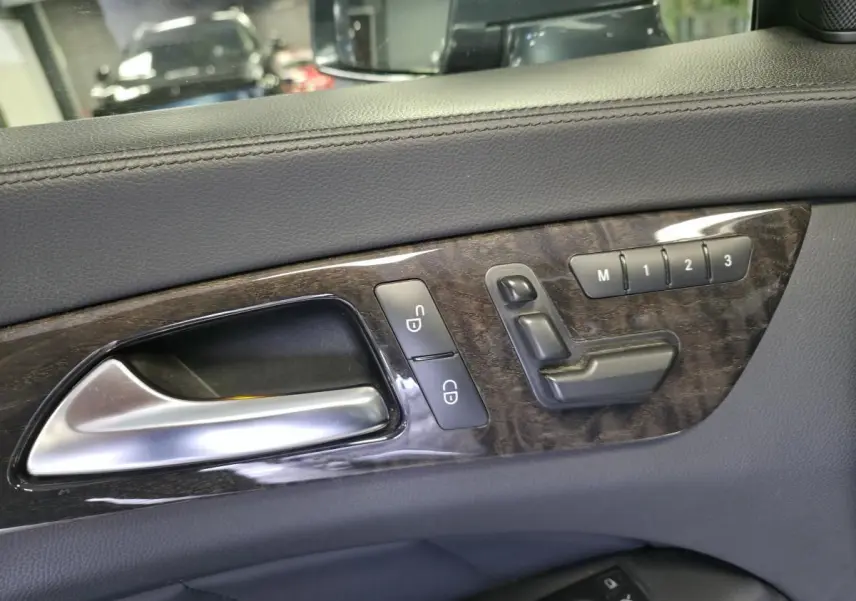 Gros plan sur la poignée intérieure et les commandes de réglage de siège en cuir gris avec insert bois d'une Mercedes CLS 250 CDI 2011.