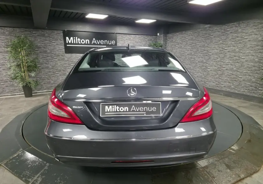 Vue arrière d'une Mercedes Classe CLS gris métallisé avec feux arrière rouges et plaque Milton Avenue dans un showroom.