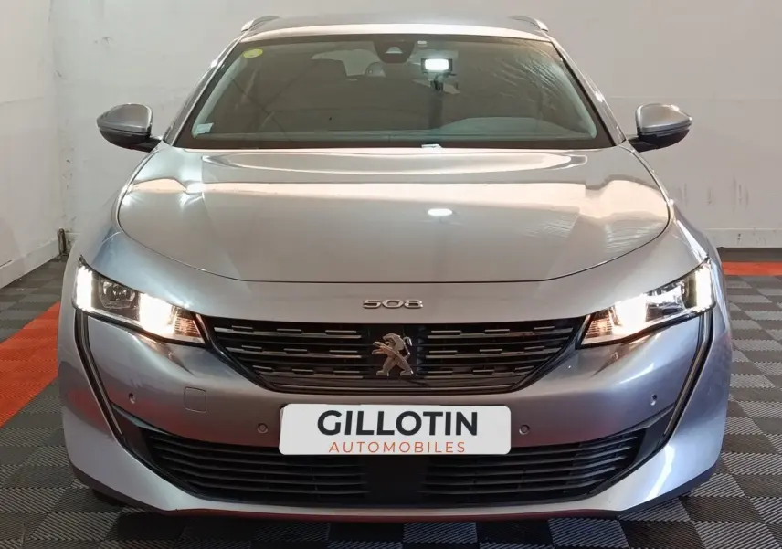 Vue frontale d'une Peugeot 508 gris clair avec phares allumés et calandre noire distinctive.