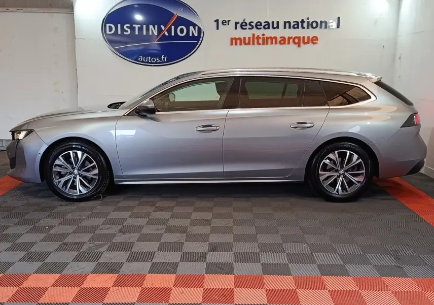Profil droit d'une Peugeot 508 SW BlueHDi gris clair 2020 avec jantes alliage et vitres teintées, en intérieur showroom.