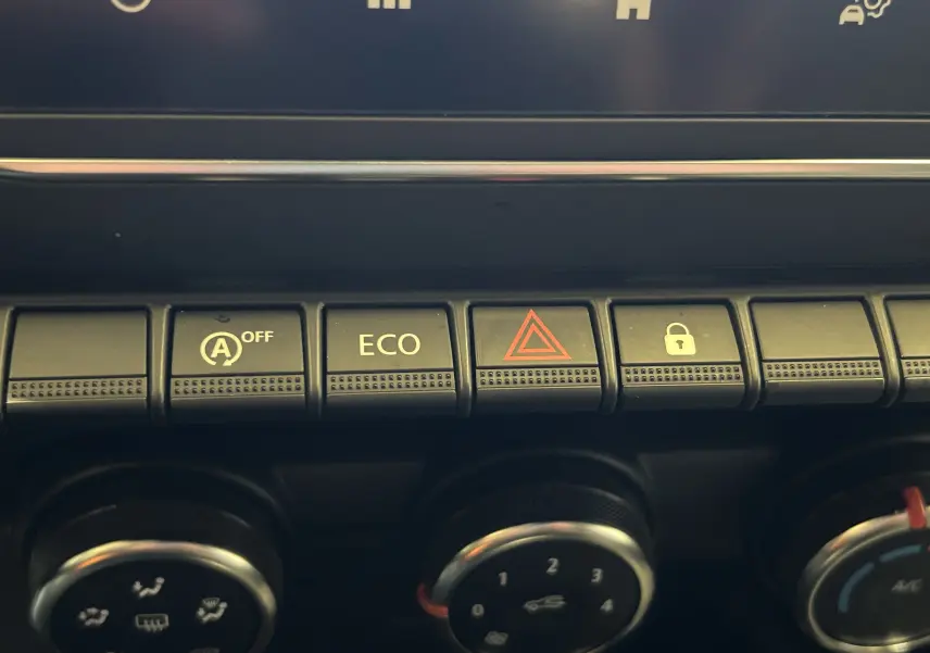 Gros plan sur les boutons de commande noirs du tableau de bord de la Renault Clio V blanche, avec touches ECO et alerte.