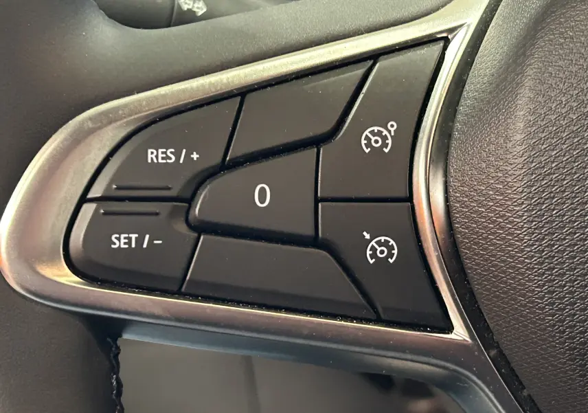 Gros plan sur les commandes de régulateur de vitesse au volant d'une Renault Clio V blanche, version BlueDCI 100 Evolution.