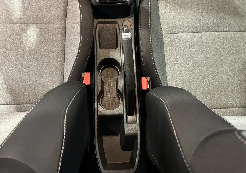 Vue plongeante sur la console centrale et les sièges tissu gris avec accoudoirs noirs de la Renault Clio V blanche.