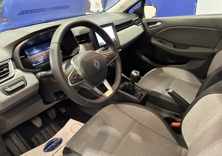 Intérieur de la Renault Clio V blanche, vue côté conducteur, volant multifonction et boîte manuelle visibles.