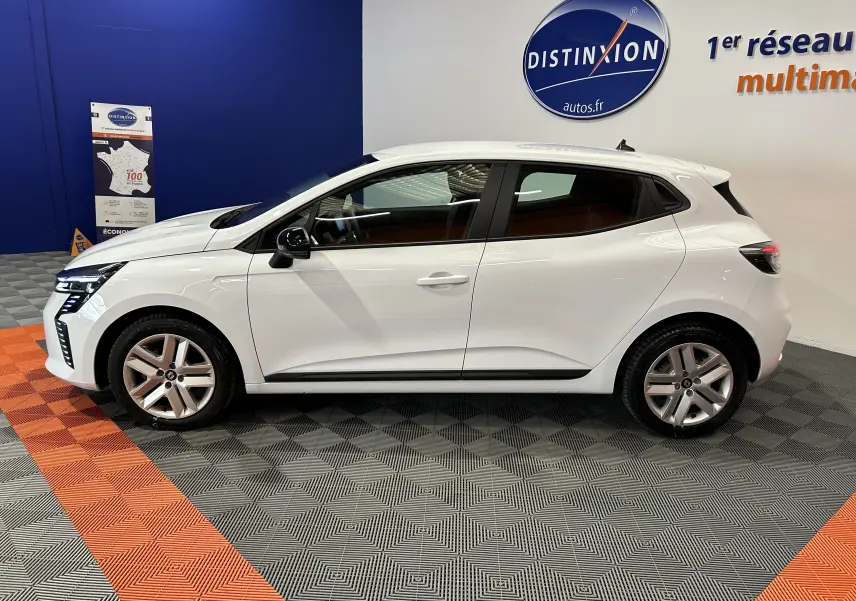 Profil côté gauche d'une Renault Clio V blanche 5 portes, vue en intérieur sur fond bleu et gris avec logo Distinxion.