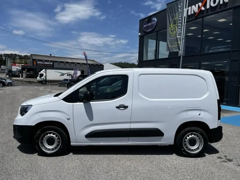 Vue de profil côté gauche d’un Opel Combo Cargo blanc 2024 stationné devant un bâtiment commercial.