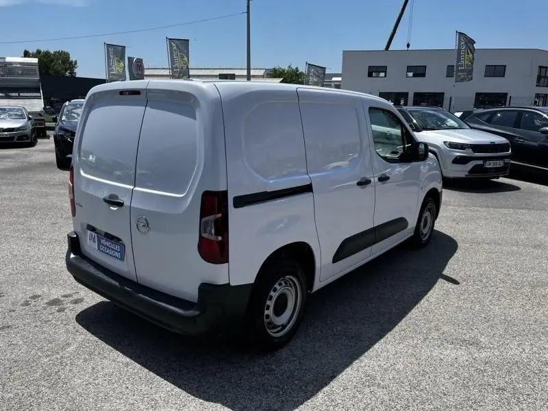 Vue 3/4 arrière droite d'un Opel Combo Cargo blanc 2024, fourgon utilitaire avec portes arrière battantes et protections latérales noires.