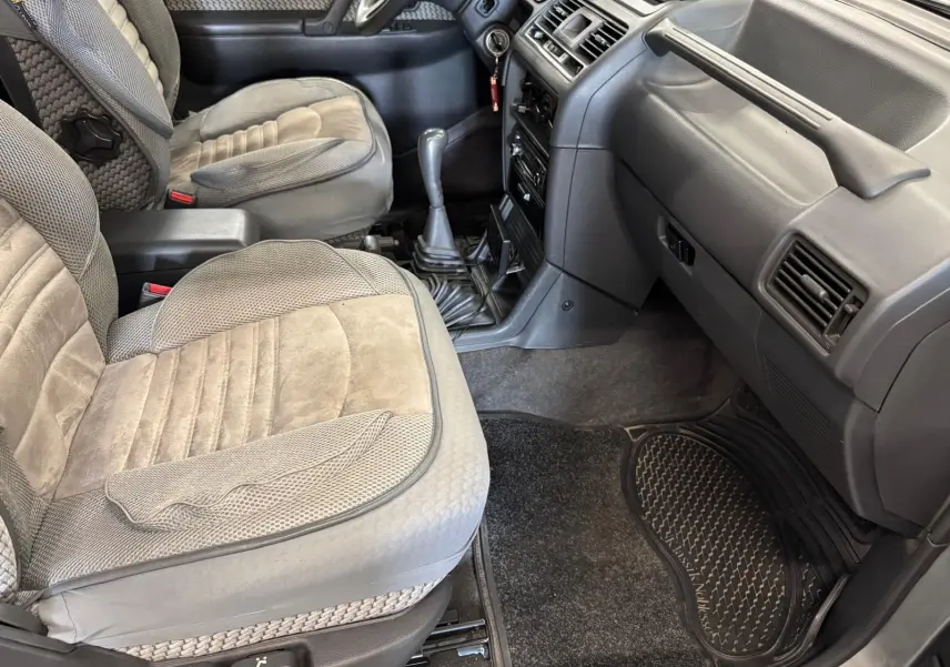 Vue intérieure côté passager du Mitsubishi Pajero Court 2.8 TD 1997 avec sièges gris et tapis en caoutchouc.