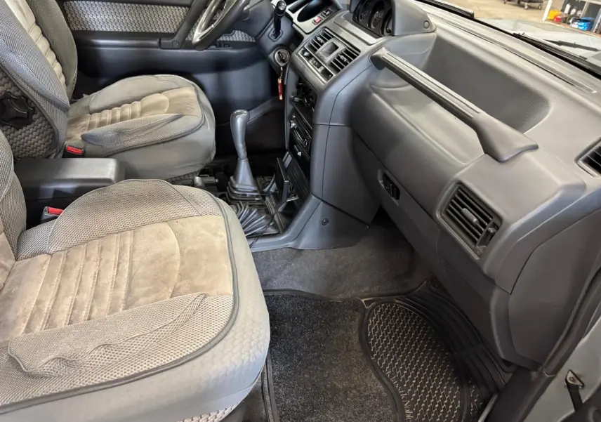 Vue intérieure côté passager du Mitsubishi Pajero Court 2.8 TD 1997 avec sièges gris et tableau de bord gris foncé.