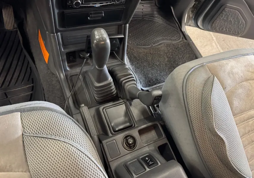 Vue intérieure centrée sur la console centrale et levier de vitesses d’un Mitsubishi Pajero Court gris aluminium de 1997.