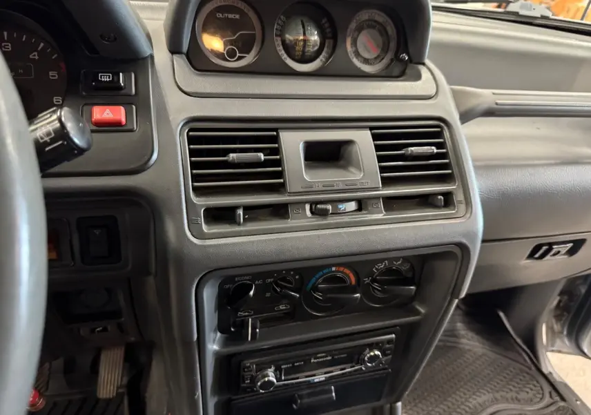 Vue rapprochée de la console centrale intérieure du Mitsubishi Pajero Court 1997, avec tableau de bord gris et commandes climatisation.
