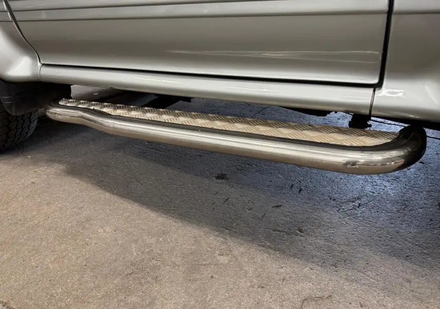 Gros plan sur le marchepied en métal strié sous la porte côté gauche du Mitsubishi Pajero Court gris aluminium.